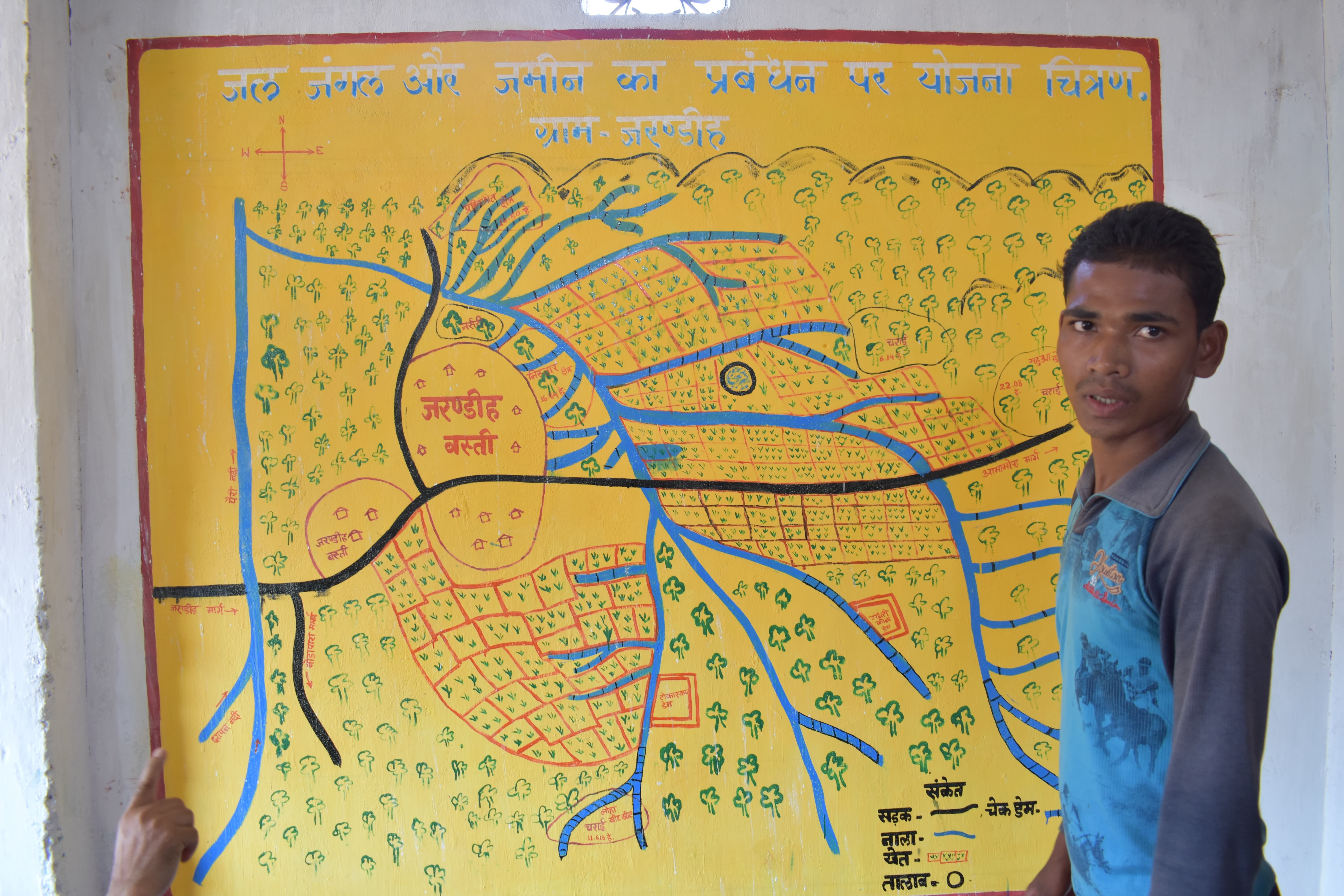 Charan Singh Sori, a youth undergoing GPS training, presenting how the village manages the community forest in front of the village resource map.